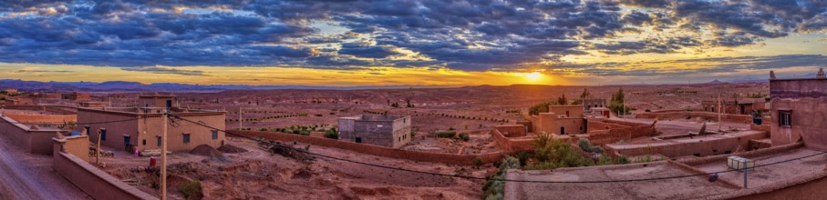 Wide desert landscape at sunset with scattered buildings and dramatic clouds, Skoura in Morocco