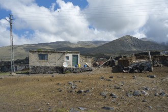 A simple stone house with power lines in a mountainous landscape, village at the foot of Great