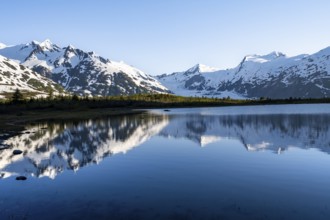 Mountain peaks with Portage Glacier glacier and snow reflected in Divide Lake mountain lake in