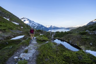 Hikers on Portage Pass, snow-covered mountains and Fjord Passage Canal, near Whittier, Alaska, USA