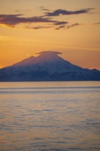 View of Cook Inlet on white mountain peaks of Mount Redoubt at sunset, picturesque golden light of