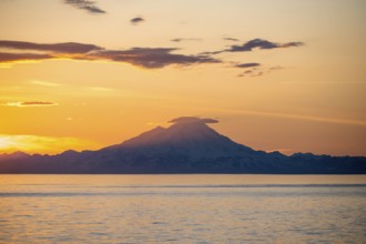 View of Cook Inlet on white mountain peaks of Mount Redoubt at sunset, picturesque golden light of