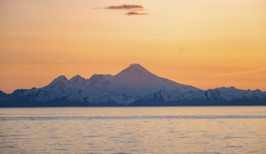View of Cook Inlet on white mountain peaks of Mount Iliamna at sunset, picturesque golden light of