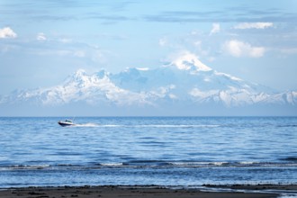View over Cook Inlet to white mountain peaks of Mount Iliamna, motor boat rides on the ocean,