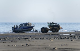 Motor boat on a boat trailer is driven into water by a tractor on a beach, Anchor Point, Alaska,