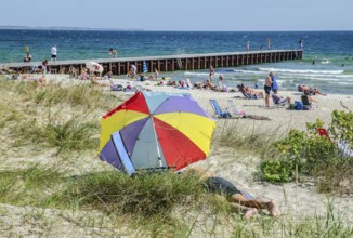 Colorful parasol on the beach with jetty and sunbathing people in Ystad, Skåne County, Sweden,