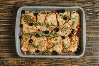 Roasted pork chops placed over a bed of colourful vegetables, garnished with olives and fresh herbs