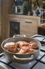 A rabbit's hind leg and saddle is simmering in a skillet, seasoned with herbs, on a gas stove in a