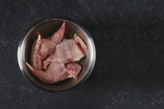 Fresh rabbit hind legs and a saddle are soaked in water with vinegar in a metal bowl. The process