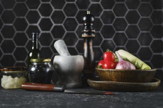 A variety of fresh vegetables such as tomatoes, onions, and greens sit on a dark kitchen counter