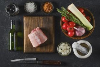 Fresh ingredients are beautifully arranged on a wooden board, including a piece of raw rabbit