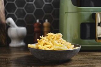 Fries are piled high in a dark bowl on a kitchen counter. The setting features a stylish air fryer