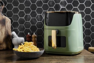 A sleek air fryer is on a wooden countertop in a contemporary kitchen. A bowl of golden, crispy