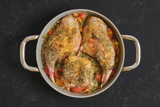 Two rabbit hind legs and a saddle are seasoned with herbs and spices, placed on a bed of colorful