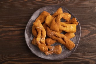Crunchy biscuit Brushwood cookies sprinkled with powdered sugar on brown wooden background, top