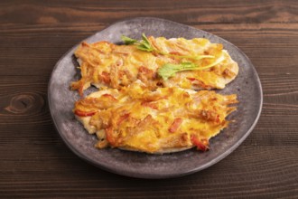 Baked chicken meat with cheese and tomatoes on brown wooden background. side view, close up