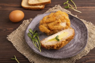 Chicken Schnitzel on gray plate with microgreen on brown wooden background and linen textile. side