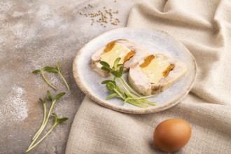 Chicken, egg and dried apricot meatloaf, microgreen on brown concrete background and linen textile.
