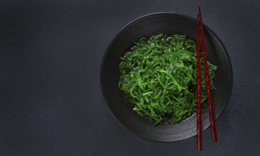 Chuka salad, made from fresh seaweed, with sesame dressing, served in a black bowl, with chopsticks