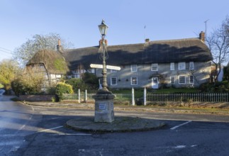 Historic signpost with direction arrows, thatched cottages in village of Pewsey, Wiltshire,