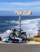 Sticker-covered sign with bicycles and surfboards, Nazaré, Portugal