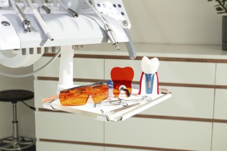 On the tray are various dental instruments, a model dental implant and bright orange safety