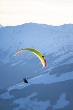 Paragliders flying over snowy mountain peaks in winter in evening light, Kitzbühel Alps, Tyrol,