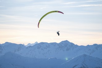 Paragliders flying over snowy mountain peaks in winter in evening light, Kitzbühel Alps, Tyrol,