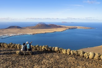 Tourists on a bench on the viewing platform at the Mirador del Río viewpoint, in the evening light,