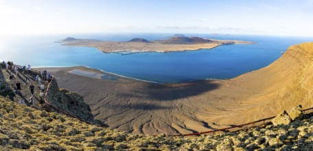 View of La Graciosa island with volcanic craters in the evening light, tourists on an observation