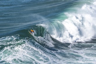Surfers with their jet ski pilots in the Atlantic waves below Farol de Nazaré, Forte São Miguel,