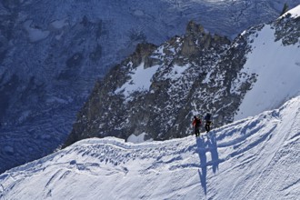 Two ascended mountaineers run across a snow-covered mountain ridge, Aiguille du Midi,