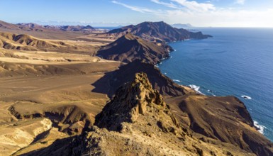 Desert landscape converges with ocean along a rugged coastal area, shore break at cliffs, blue