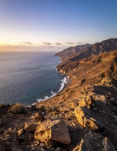 Desert landscape converges with ocean along a rugged coastal area, shore break at cliffs, blue