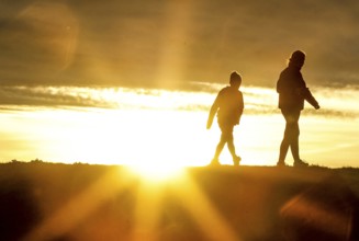 Woman and child walk across a dike on the island of Fehmarn at sunset, 13.10.2025, Fehmarn,