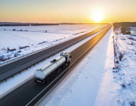 Petrol cargo truck lorry tanker driving on highway hauling oil products at sunrise, wide snowy
