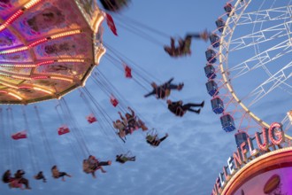 An illuminated chain carousel turns at night at a funfair, with floating people and colourful