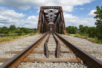 Railroad tracks leading to old rusted Terrebonne Pratt truss railroad bridge over Des Mille-Iles