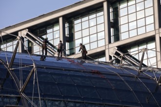 Three male glass cleaners abseiling down a glass roof of Berlin Central Station to clean windows,