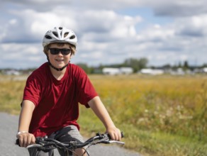 A boy with a bicycle helmet rides a bicycle and smiles friendly into the camera, AI generated, AI