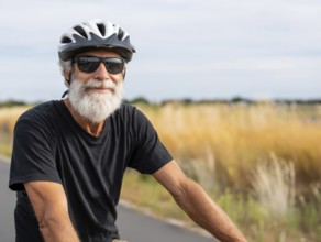 A man, senior citizen with a bicycle helmet rides on a bicycle and smiles friendly into the camera,