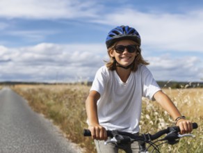 A girl with a bicycle helmet rides a bicycle and smiles friendly into the camera, AI generated, AI