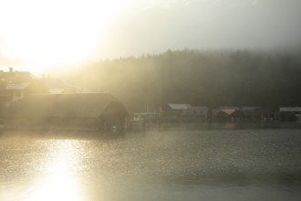 Mystical morning at Königssee in Schönau with boathouses. Sunrise and beautiful wafts of mist over