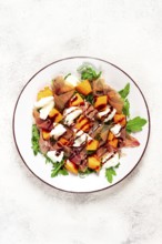 Salad with slices of ripe melon, prosciutto, mozzarella and fresh arugula, decorated with balsamic