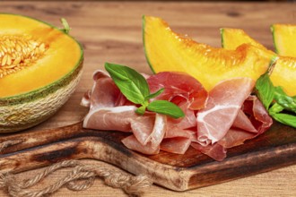 Cantaloupe melon, with prosciutto, and fresh basil, on a wooden serving board, rustic style