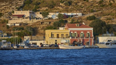 Harbour town with colourful buildings on the waterfront and hills in the background at sunset, Agia