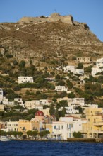 Panteli Fortress, White houses stretch along a hill with a fortress at the top and the sea in the