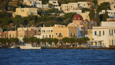 Colourful coastal houses and church by the sea with trees, sunny Greek town view, Agia Marina,