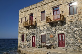 Stone house with red windows and balconies right on the waterfront in sunny weather, Agia Marina,
