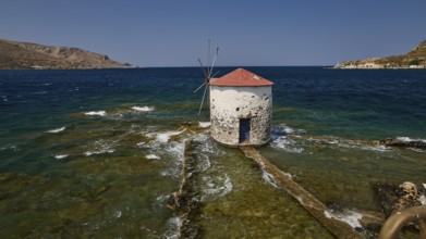 Historic windmill stands in the turquoise sea, surrounded by waves and a clear sky, Agia Marina,